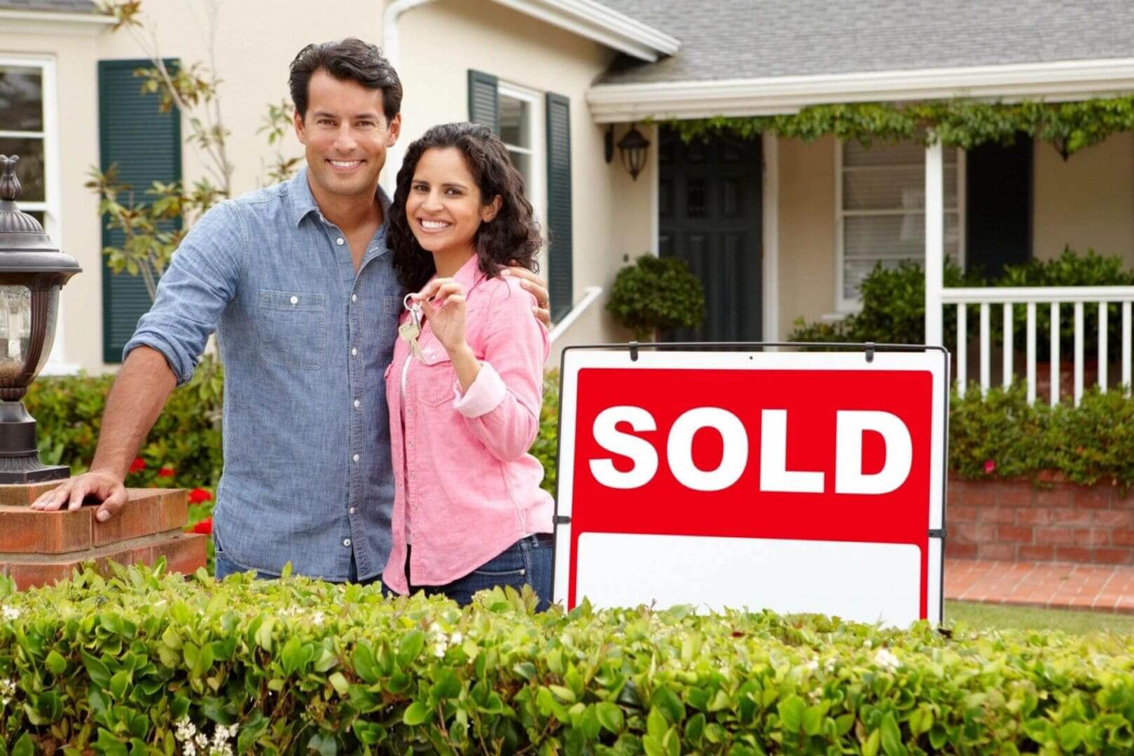 A couple standing in front of their home with the sold sign.